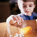 Photo of a young boy leaning over a table where a bottle of pills has been opened with contents spilled across the table.