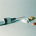 Syringe against white background with several, unnamed pills scattered around it.