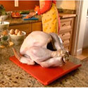 Uncooked turkey sitting on kitchen counter while woman washes her hands in the background.