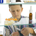 Young boy stands in front of open medicine cabinet looking at rows of medicine bottles.